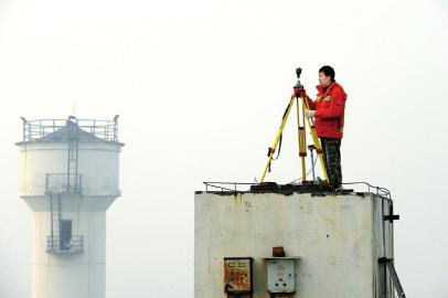 一位工作人员在川师附中楼顶的成都地铁GPS坐标点上工作，未来开通的7号线就是靠这些坐标点来确定位置施工的。